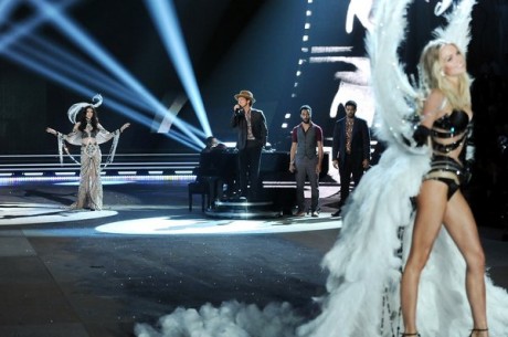 Singer Bruno Mars center performs while a models walk the runway.